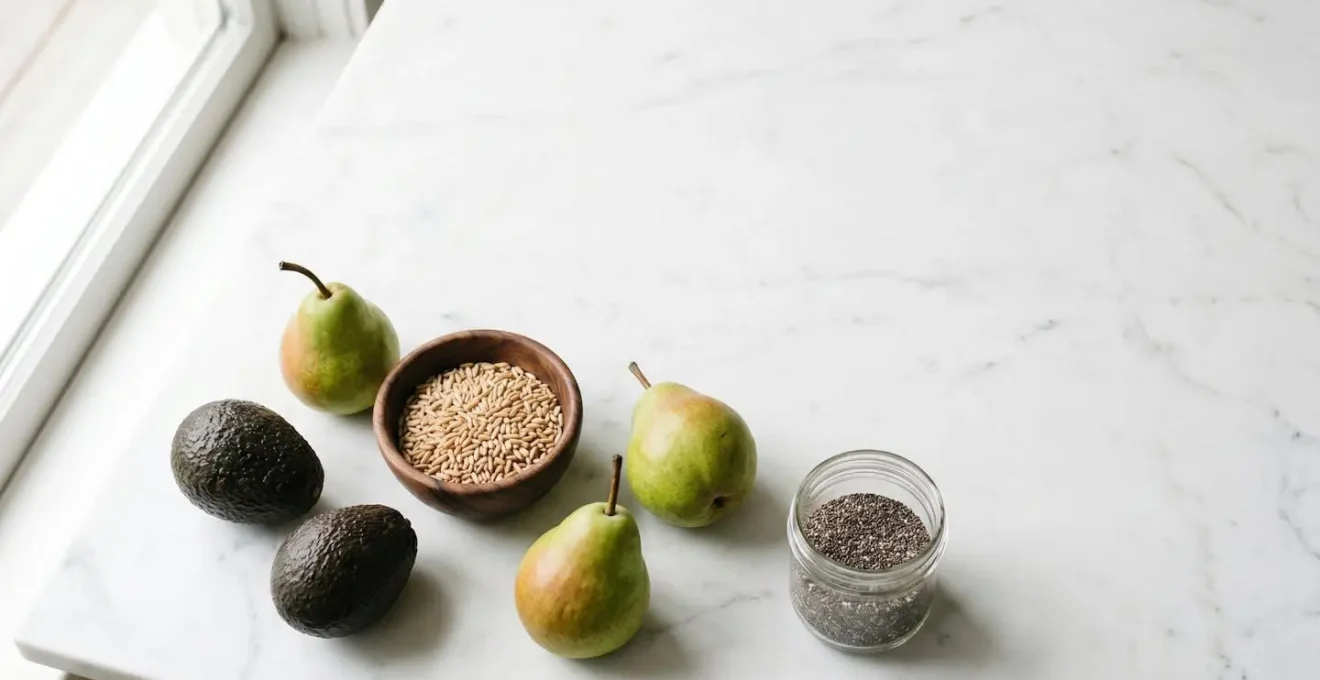 Wide environmental shot of whole soluble fiber foods including oats, pears, and avocados arranged naturally on clean white surface with generous negative space